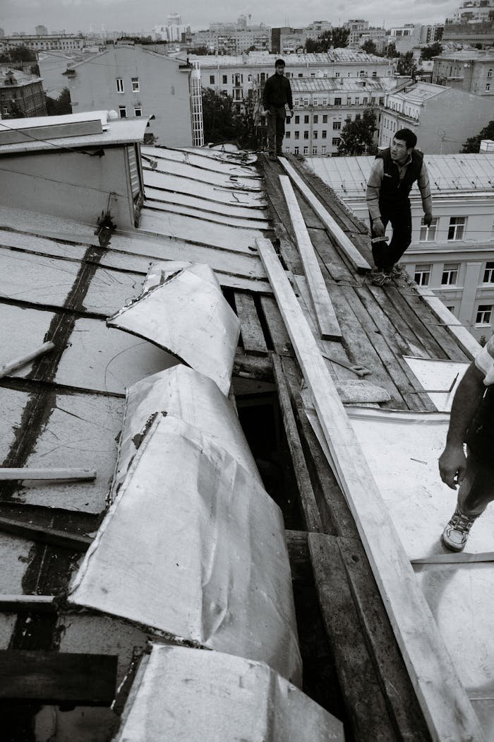A group of workers repairing a damaged urban rooftop from a high angle.